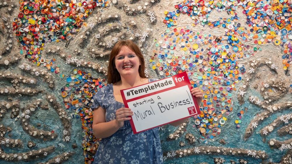 Abigail McNavage holding a #TempleMade sign in front of her painting 