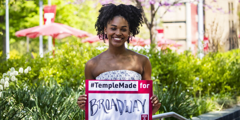 Jasmine Villaroel holding a Temple Made for sign outside on Main Campus