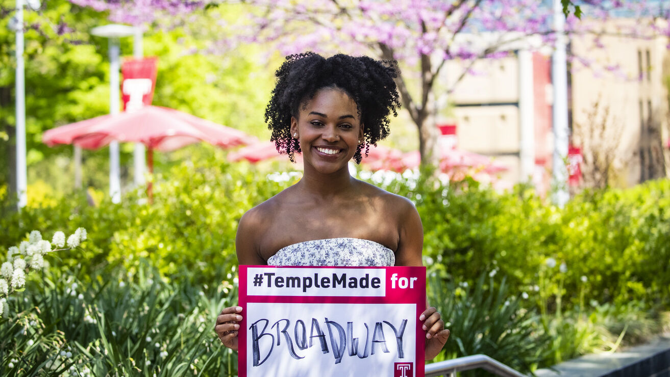 Jasmine Villaroel holding a Temple Made for sign outside on Main Campus