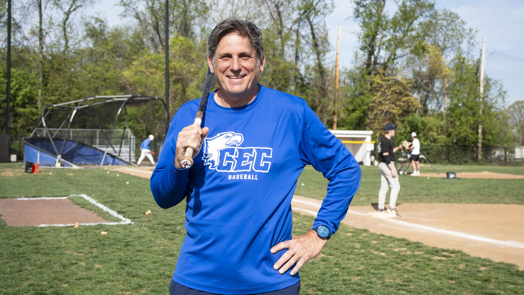 Image of a person wearing a blue shirt and holding up baseball bat on a field.     