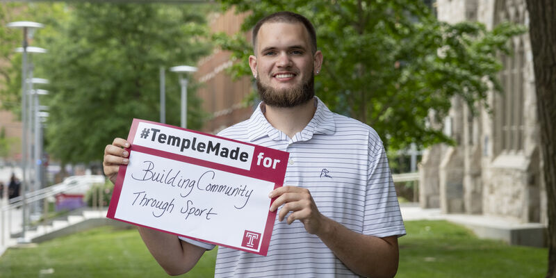 Ezekiel Cartwright standing outside holding up a Temple Made for sign    