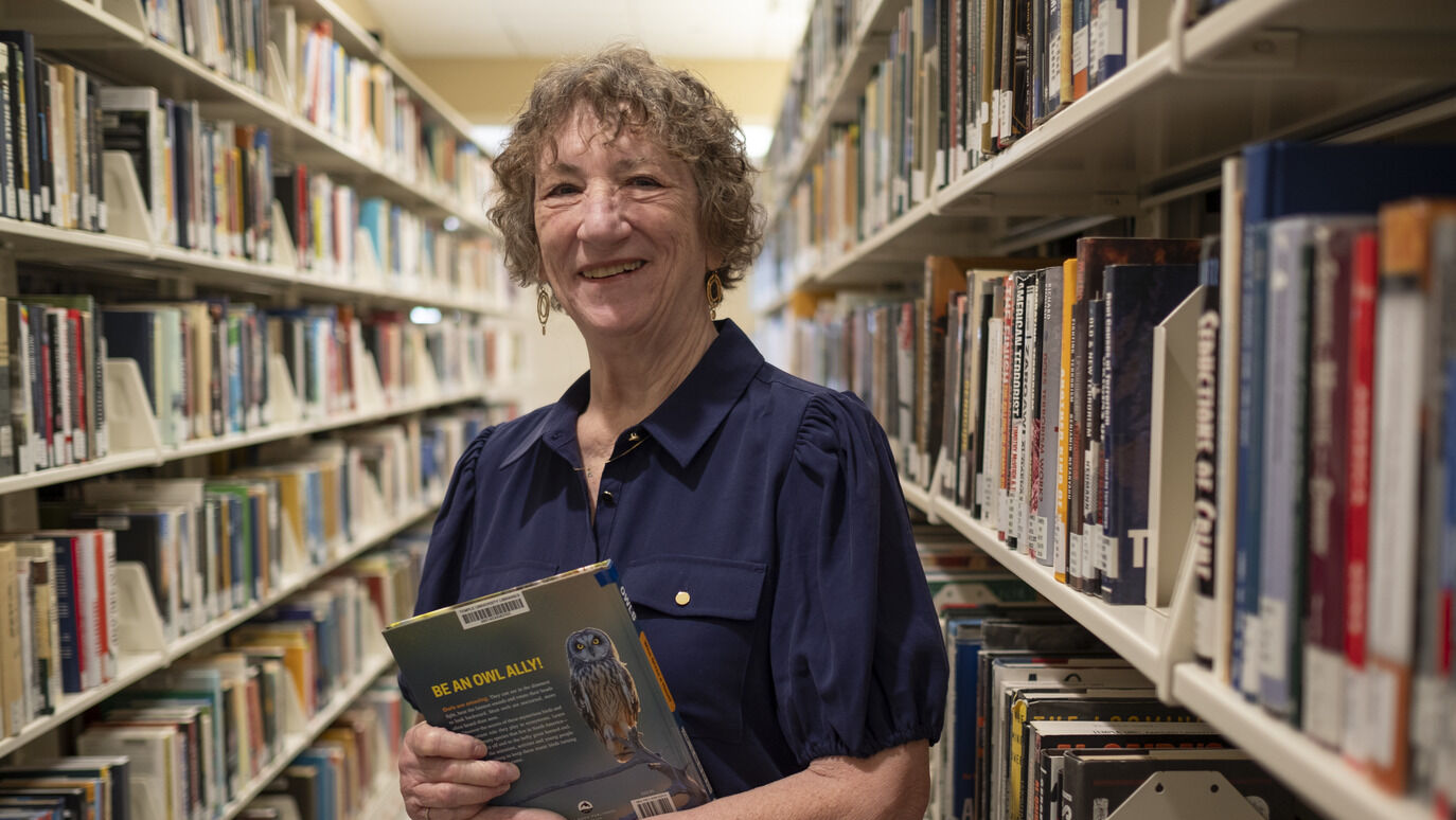 Sandi Thompson standing in the book stacks with a book in her hands at Ambler Campus Library