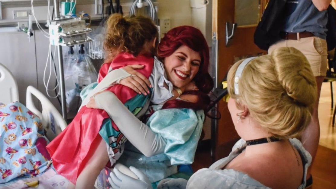 The Mermaid Princess smiles as she hugs a child in a hospital room