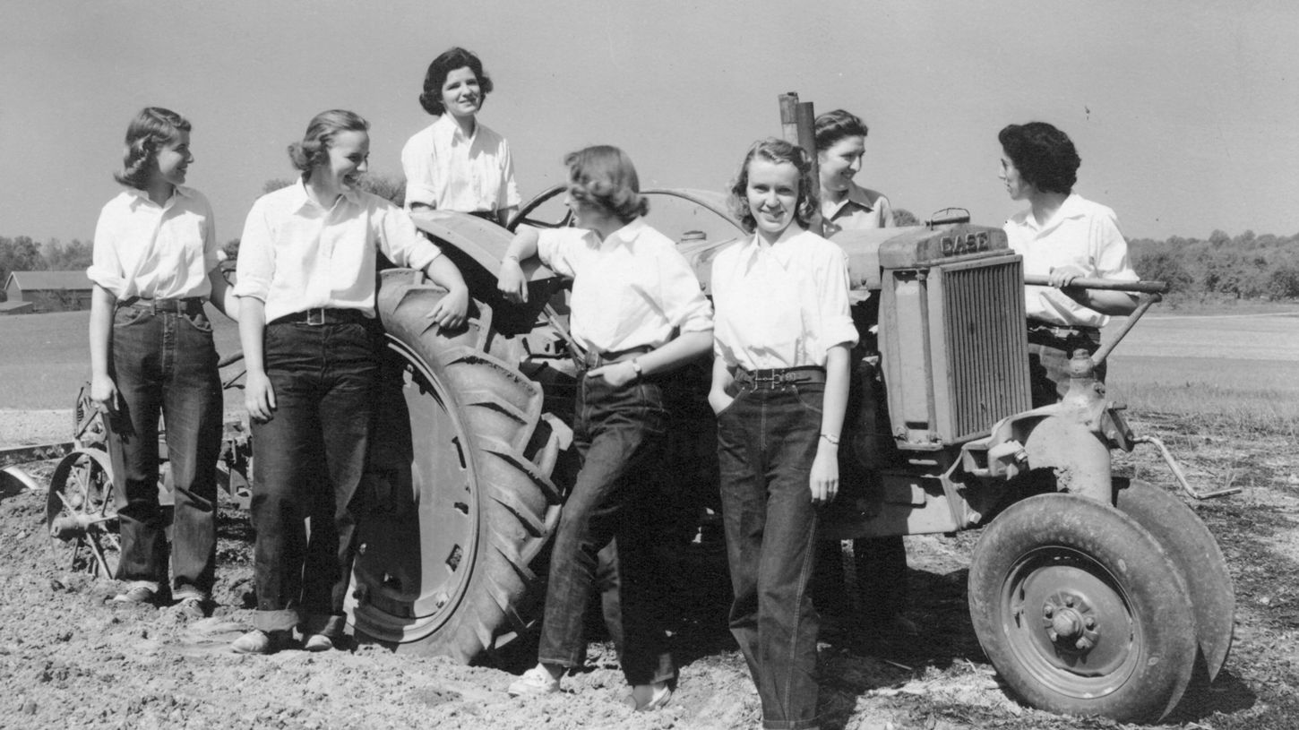 A black and white photograph of women in horticulture standing around a tractor in the field.