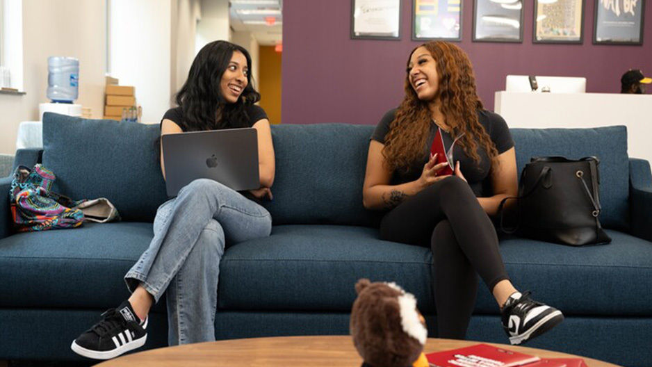Two Temple students sitting on a couch laughing.