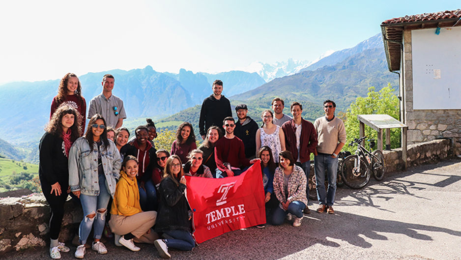 Mountains in the background, a group of Temple students holding a Temple cherry flag.