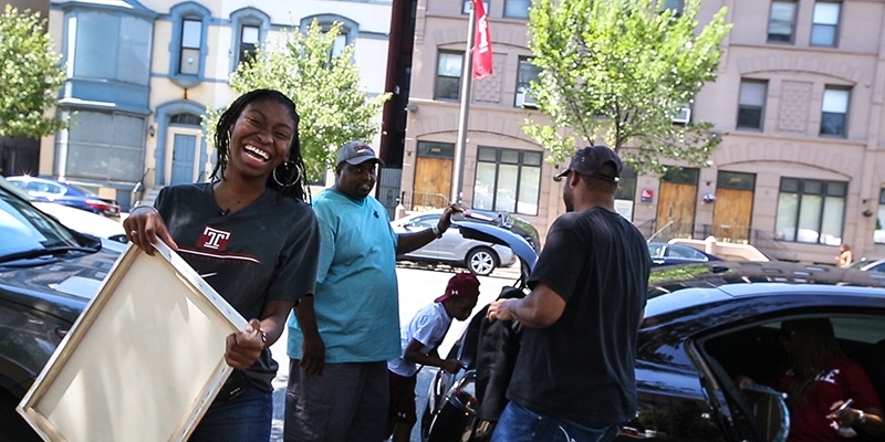 A woman in a Temple T-shirt smiling as she unpacks a car during move in.