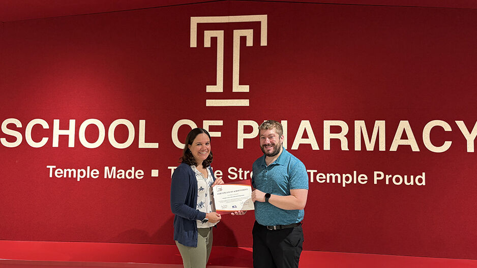 Faculty co-advisors in front of a red wall with the Temple T and the award