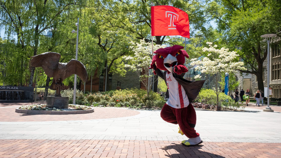 Hooter carries the Temple flag as he runs past the owl statue and points at the camera