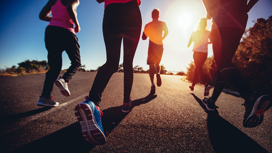 Four people’s legs as they jog on a street.