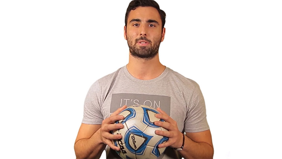 A male Temple soccer player wearing a gray T-shirt and holding a soccer ball.
