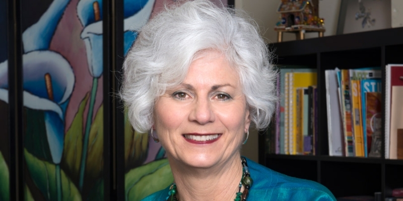 Lisa Kay wearing a teal jacket and standing in front of a bookcase.