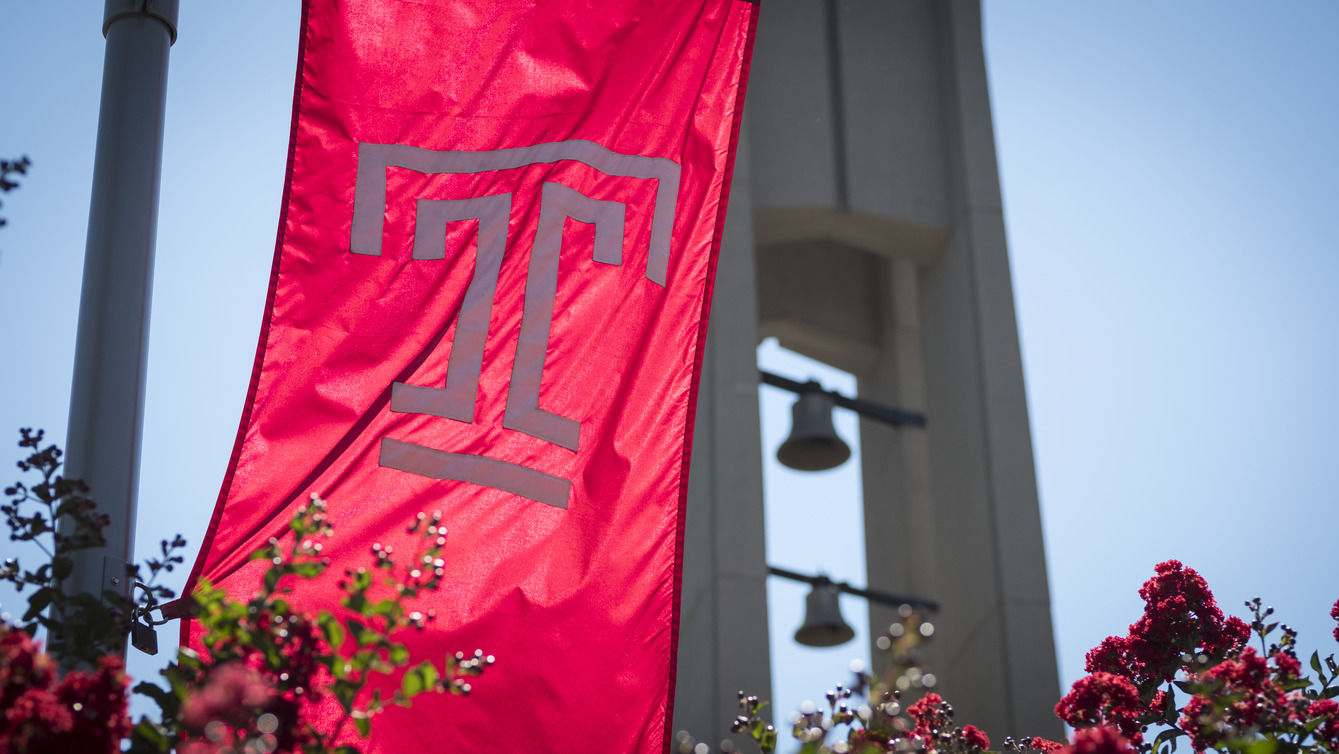 the Temple T flag waving in front of the bell tower on a clear, sunny day.