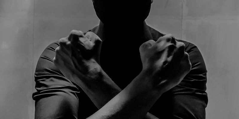 A black and white image of a man crossing his wrists over his chest in the Wakanda Forever gesture.
