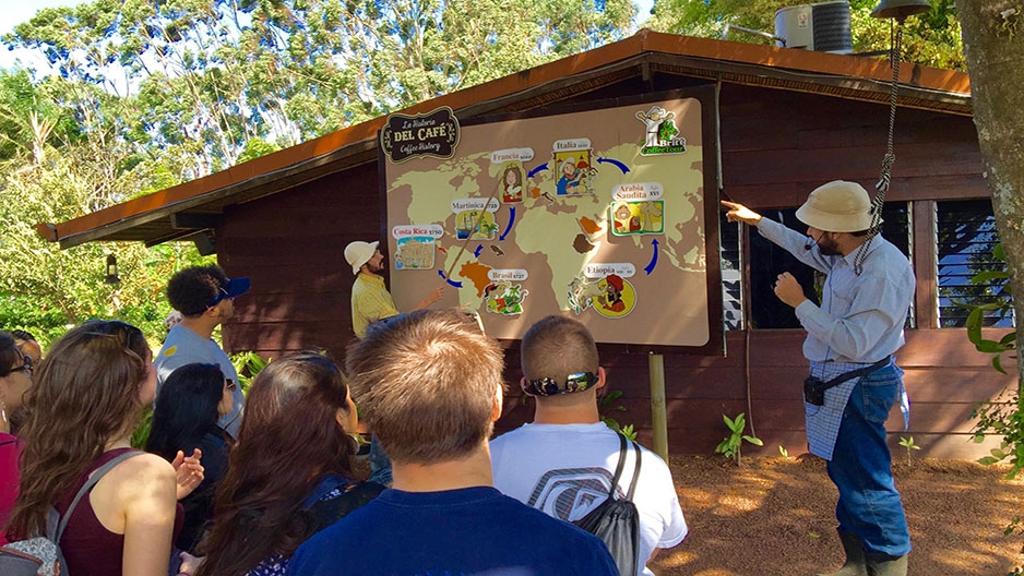 A man outside showing students a large map of the world.
