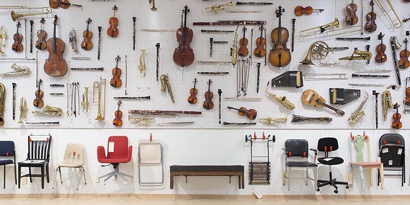 A large display of musical instruments and chairs hanging on a gallery wall. 