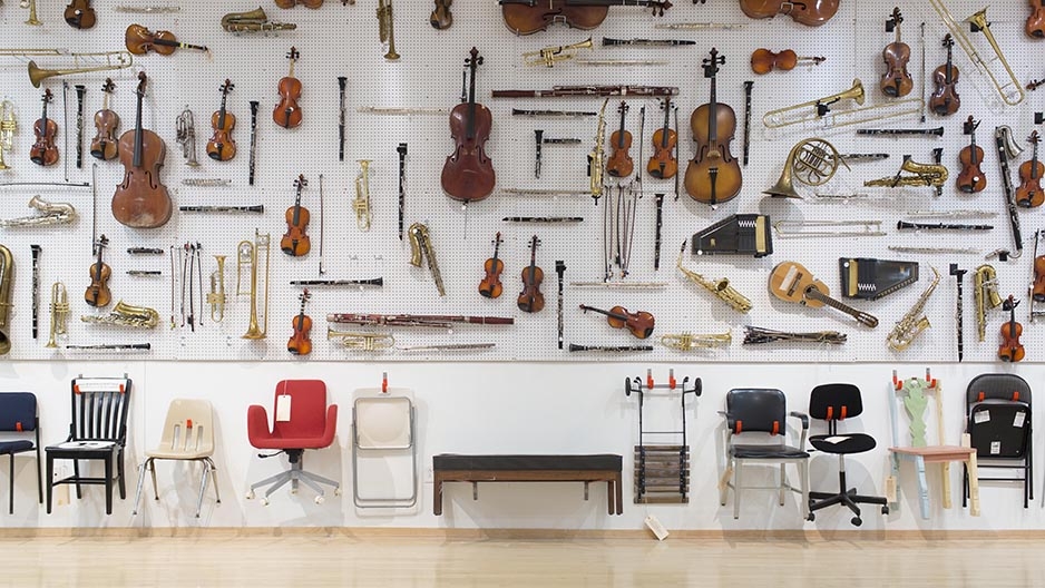 A large display of musical instruments and chairs hanging on a gallery wall. 