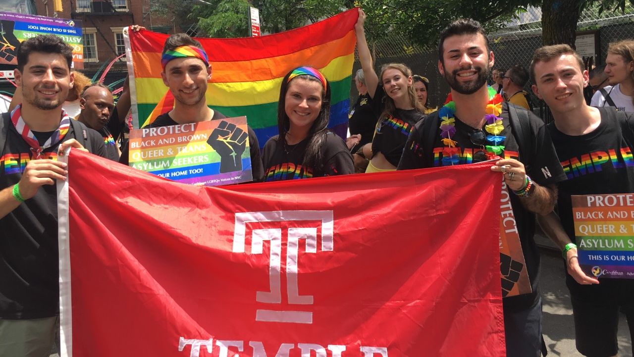 Students and alumni carrying a rainbow Pride flag and a Temple Flag.