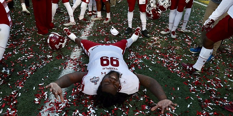 A Temple football player laying on the confetti covered field.