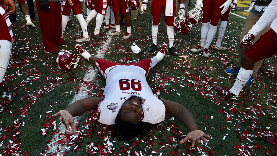 A Temple football player laying on the confetti covered field.