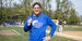 Image of a person wearing a blue shirt and holding up baseball bat on a field.