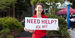 Student in a red polo holds a sign saying "Need help? Ask me!"