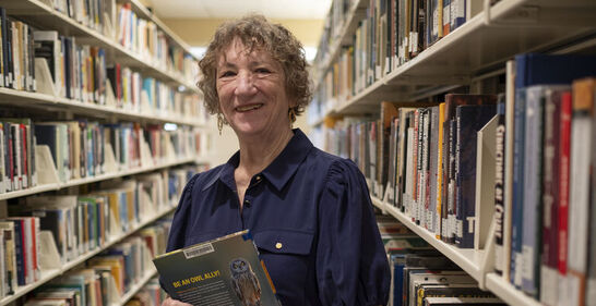 Sandi Thompson standing in the book stacks with a book in her hands at Ambler Campus Library