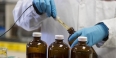 A scientist’s hand dropping liquid into test bottles.