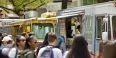 A crowd of people in front of a row of food trucks on campus. 