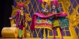 Three opera singers wearing brightly colored costumes and wigs performing on stage.