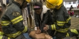 two firefighters teaching a female student how to perform CPR.