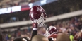 A Temple football helmet held high above a crowd of football players. 