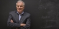 Thomas Edwards standing in front of a chalkboard with his arms crossed. 