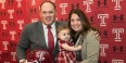 Geoff Collins holding a Temple helmet and smiling with wife and baby daughter.