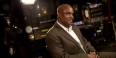 A man in a brown suit sitting in a recording studio. 