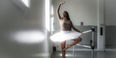 A Black woman in white tutu practicing ballet at a barre in a dance studio.