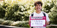 Image of Tran holding a sign that says “#TempleMade for travel and tech”