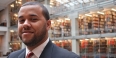 Nyron Crawford wearing a suit and tie with bookshelves in the background. 