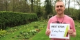 A man in a garden holding a sign that reads Next Stop: Kimley Horn.