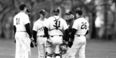 An older man with a group of student-athletes wearing caps, in black and white uniforms, standing on a raised dirt area at a Temple baseball game. 