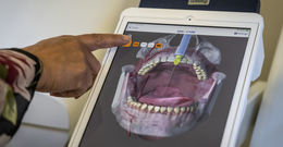 A finger points at a digital model of a mouth on a screen 
