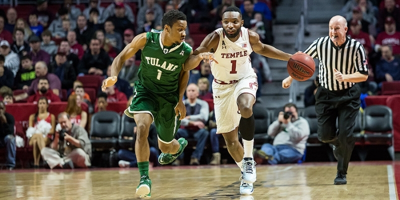 A Temple men’s basketball player dribbling a ball as a Tulane player defends.