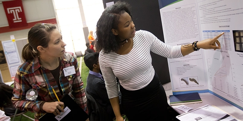A student pointing to research published on her poster at the science fair.