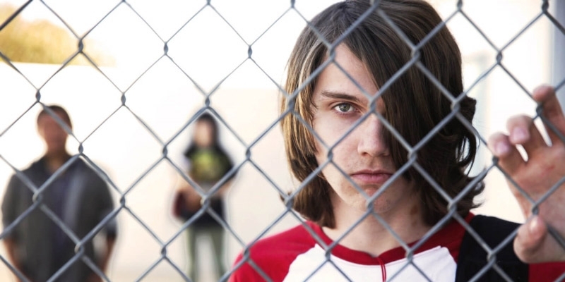 A male teen from the documentary ‘The Bad Kids’ holding a chain link fence.