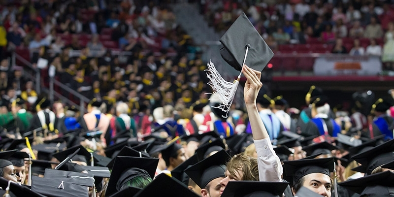 A Temple graduate triumphantly raising his cap at commencement.