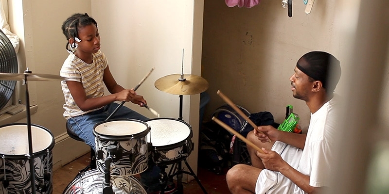 Quest Rainey teaching a young girl to play drums.