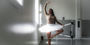 A Black woman in white tutu practicing ballet at a barre in a dance studio.