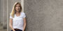 Jennifer Pollitt standing in front of a concrete building, wearing a white t-shirt.