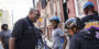 A smiling man in a black shirt with three happy children wearing helmets, sitting on bicycles during a Temple Urban Bike Team practice. 