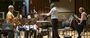 Image of Matthew Levy soloing with the wind symphony. Patricia Cornett conducts while Emma O'Halloran observes.